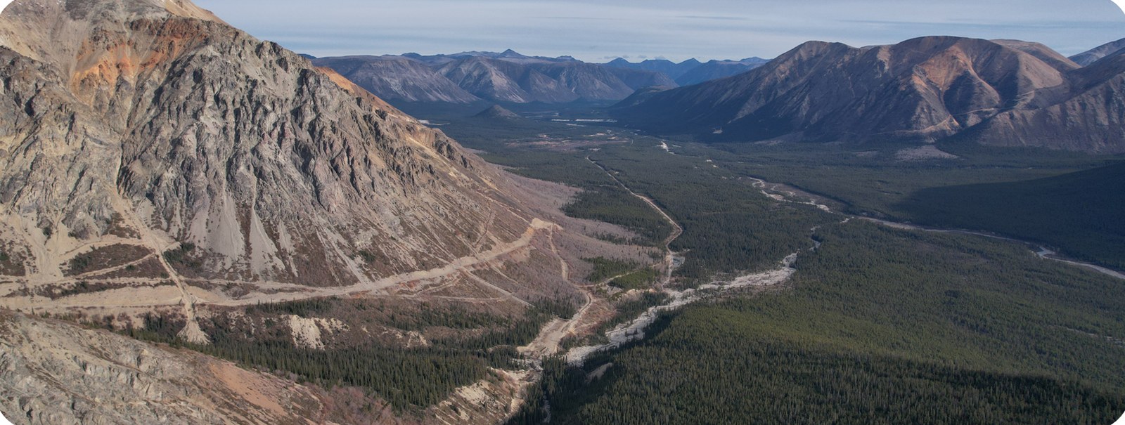 Aerial view over the Blue Jay Gold project valley, with access roads cutting through boreal forest below mineralised ridges
